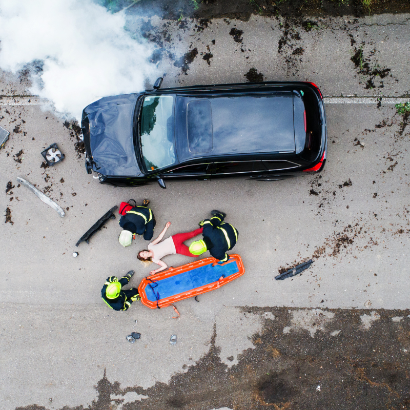 Firefighters care for an injured woman beside a crashed car, seen from above